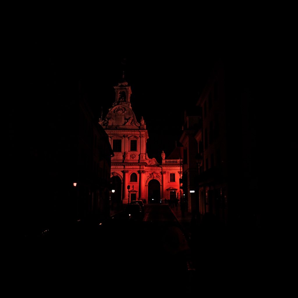 Dark, atmospheric photograph of a city square at dusk with deep shadows and muted warm lighting