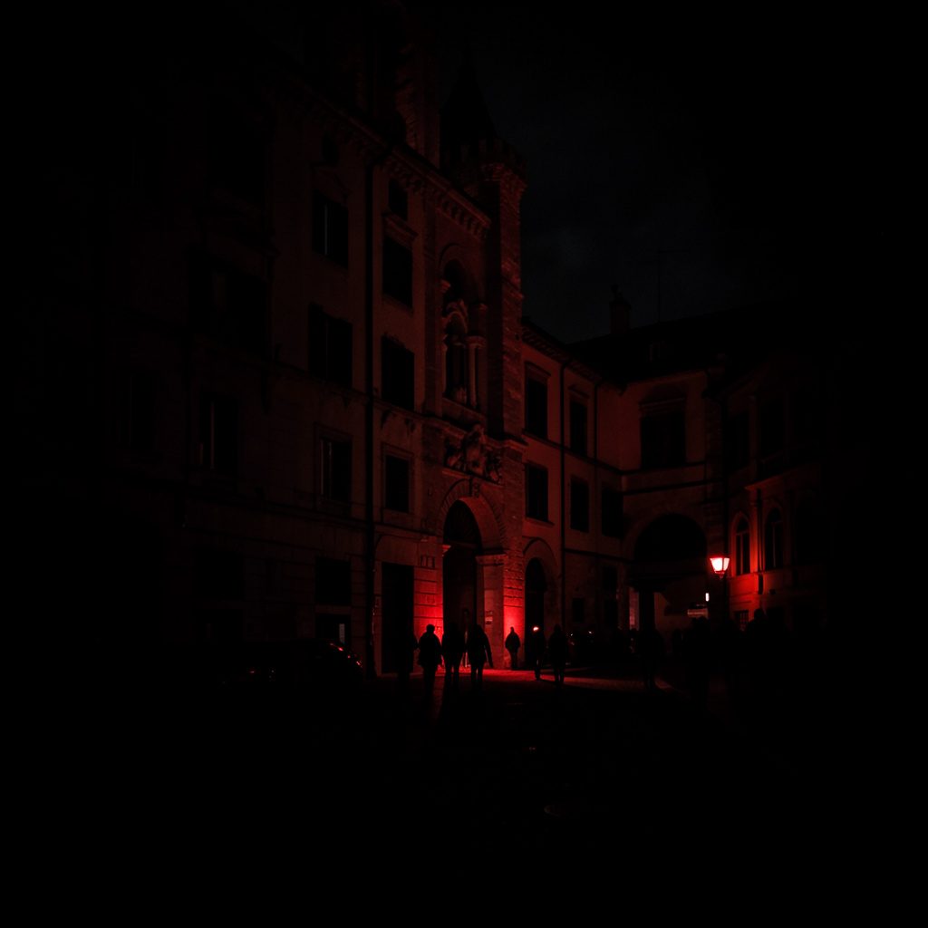 Dark, low-key cityscape photograph of Turin at dusk, deep shadow and muted red-orange highlights.